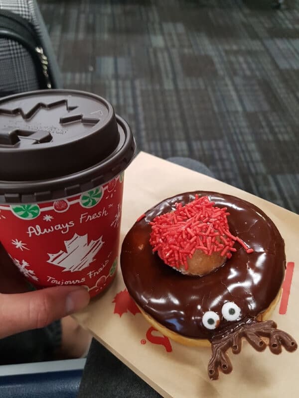 I am holding a Tim Hortons cup with white hot chocolate in it and a Christmas donut decorated to look like a reindeer 