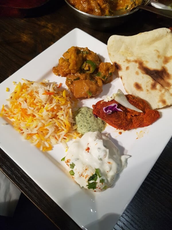 a plate full of Indian food: rice, raita, naan bread, aloo gobi, and chicken tikka masala