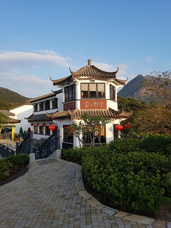 a photo of the tea place with mountains and blue sky in the background. The building has a temple like appearance 