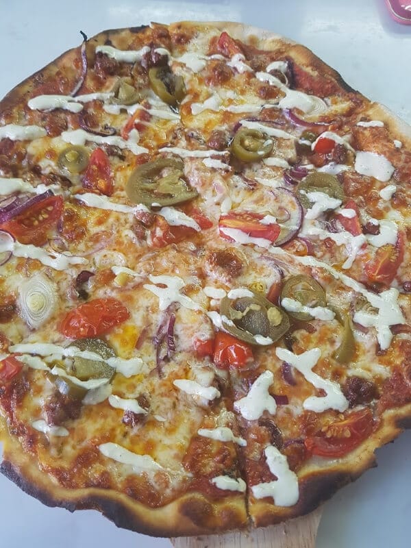 pizza with lamb, tomatoes, red onions, and jalapeno aioli drizzled on it 