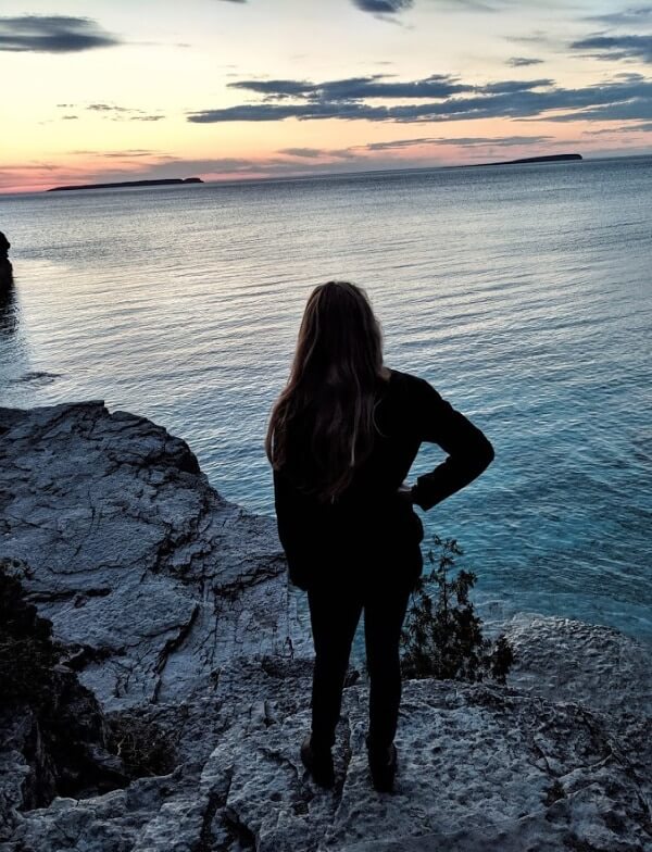I am standing on the edge of a cliff looking at the sunset. The water is clear and the sky is colorful 