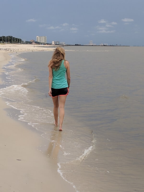 A blonde girl is walking beside the ocean in Biloxi Mississippi. 