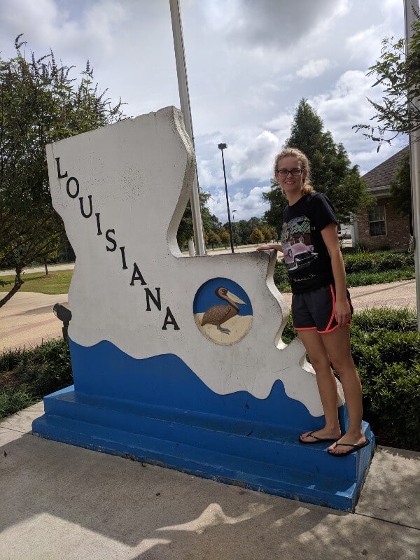 A girl is standing beside the Louisiana welcome sign.