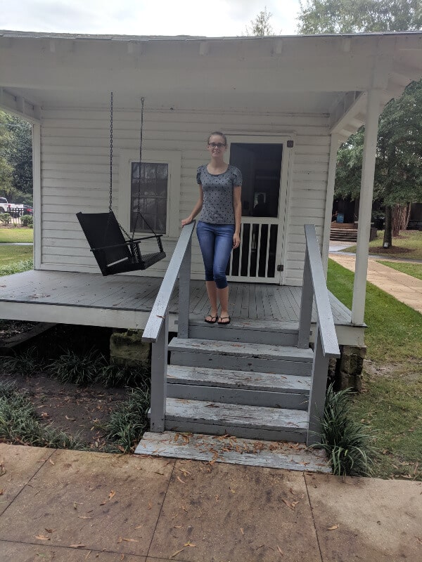 A girl is standing on the porch of a small house that was the birth place of Elvis Presley. 