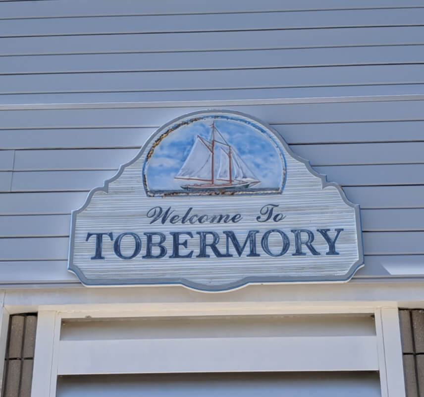 A welcome to Tobermory sign on the side of a building. The lettering is blue and above it is a picture of a boat.