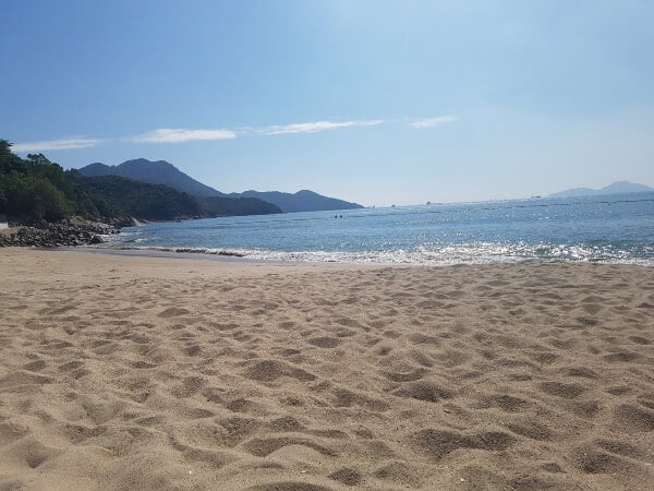 a view of the ocean as seen from the sand, mountains and rocks are on the left side 