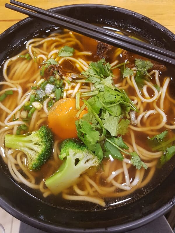 a bowl of noodles with beef, broccoli, carrots, cilantro and green onion  