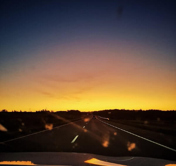 A sunrise captured from the passenger seat, the sky is blue, purple, pink, yellow and orange 