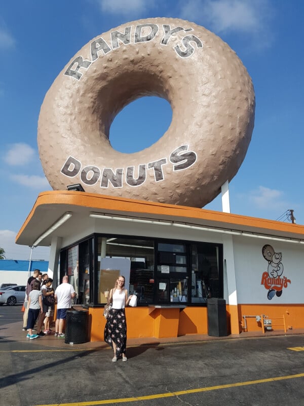 Southern California Itinerary: I am standing in front of the Randy's Donut sign with my donuts and drink