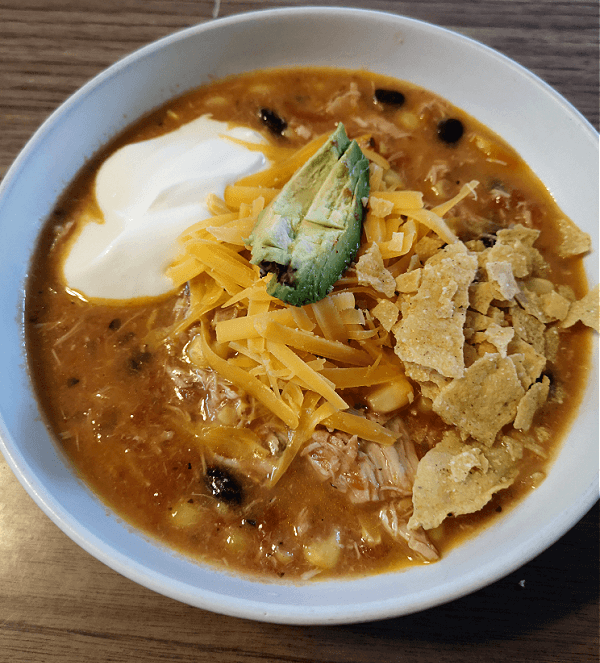 a bowl of Easy Instant Pot Chicken Tortilla Soup topped with cheese, sour cream and avocado 