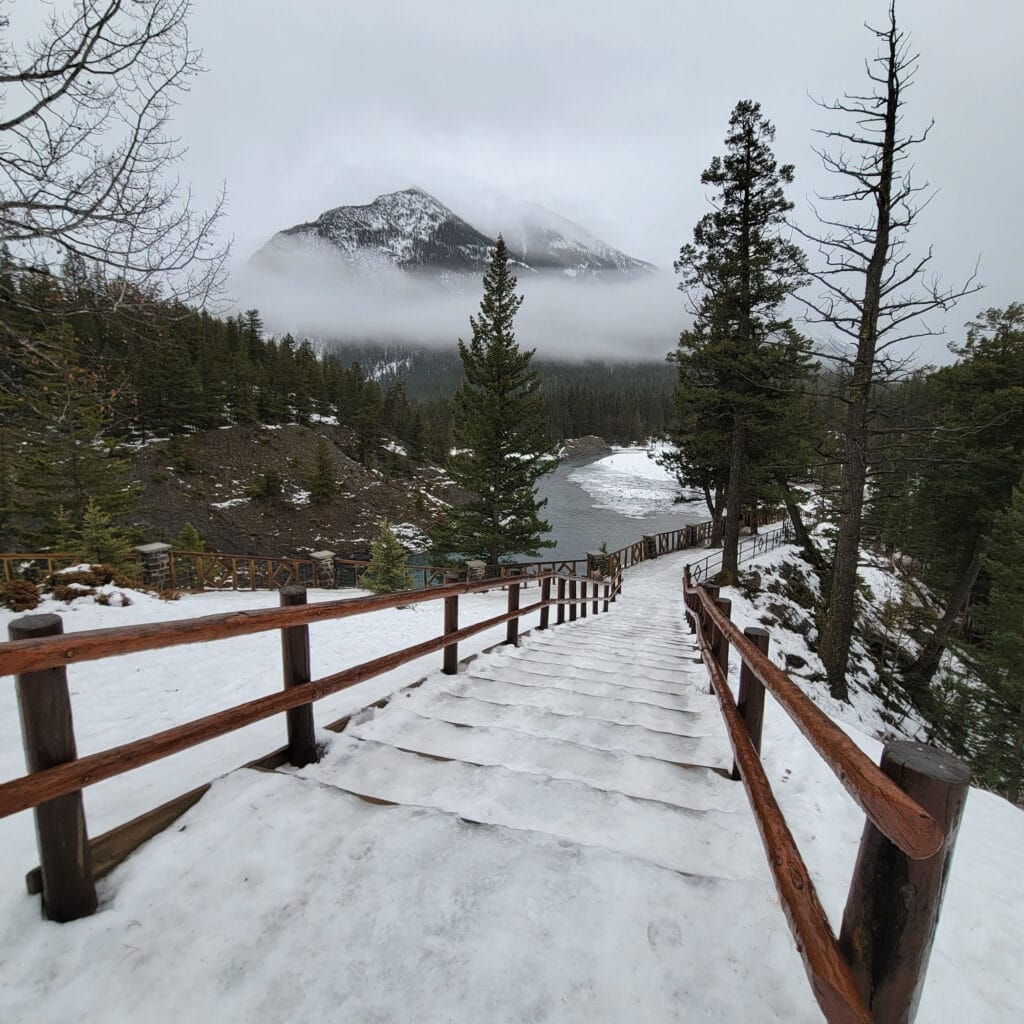 View from the top of the stairs at Bow Falls. The mountains are in the background and down below you can see Bow Falls and the river. The stairs are steep and covered in ice.