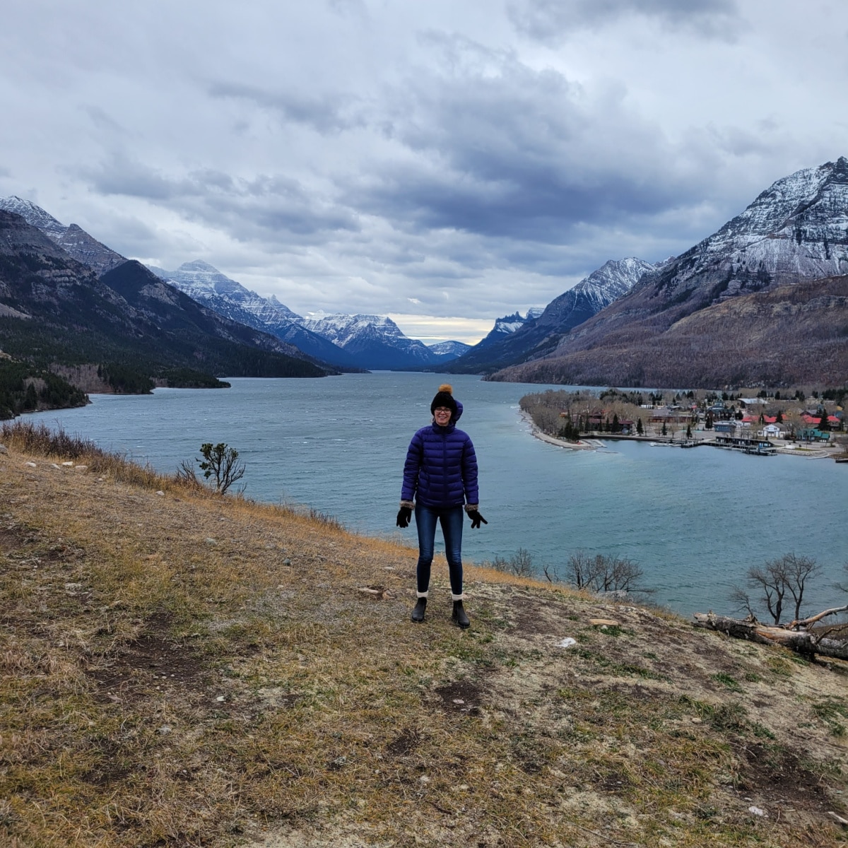 I am standing on the edge of a cliff In Waterton National Park with mountains and a lake in the background.