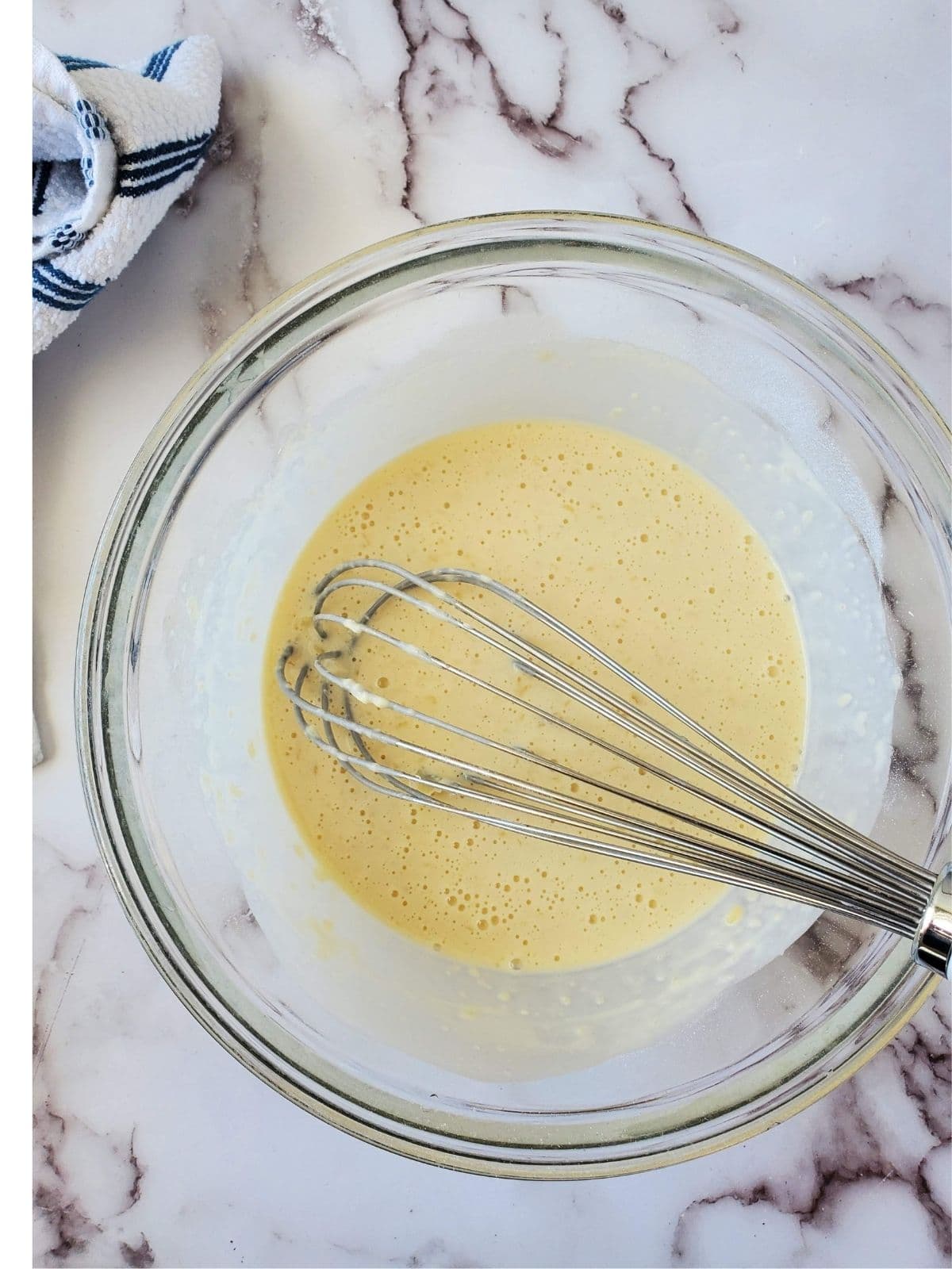 A glass mixing bowl with Belgian pancake batter and a whisk in it.