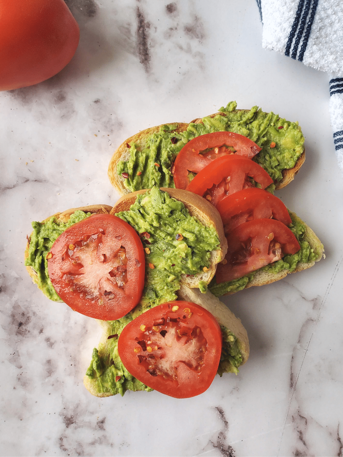 Two slices of toast with avocado and sliced tomatoes on them, sprinkled with chili flakes.