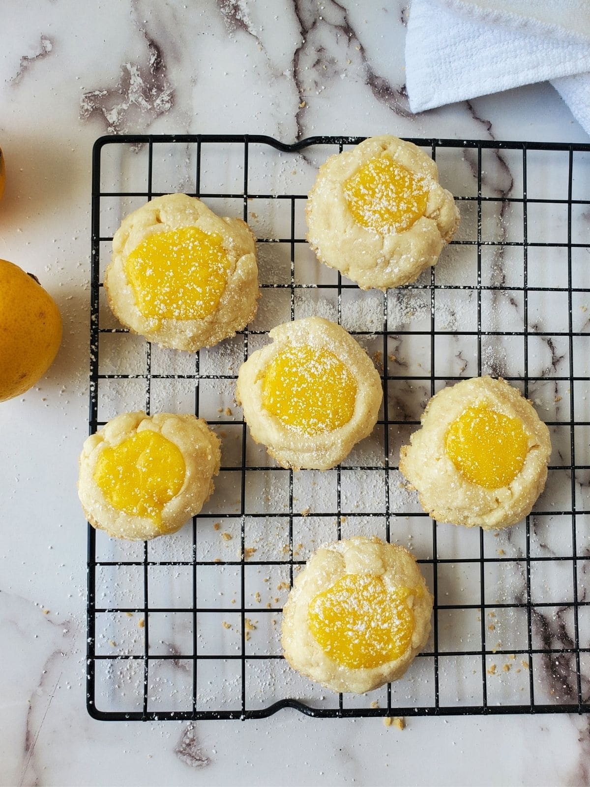 A wire rack filled with lemon curd cookies. The cookies are dusted with powdered sugar.