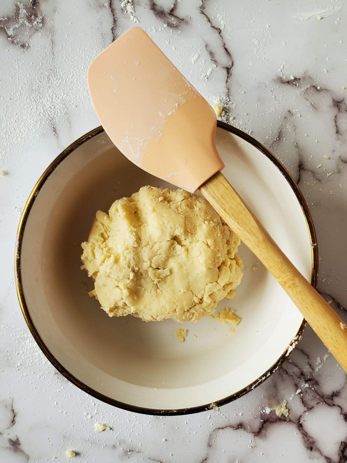 A bowl full of cookie dough for lemon curd cookies. A spatula is resting on the rim of the bowl.