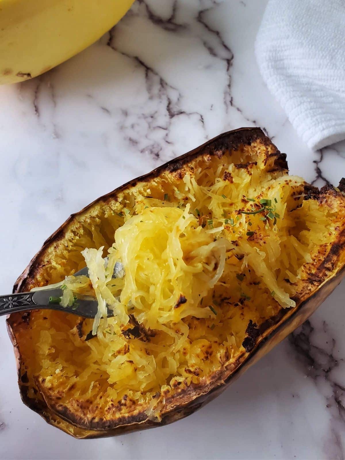 A spaghetti squash cooked in the air fryer with a fork scooping up some of the squash. 
