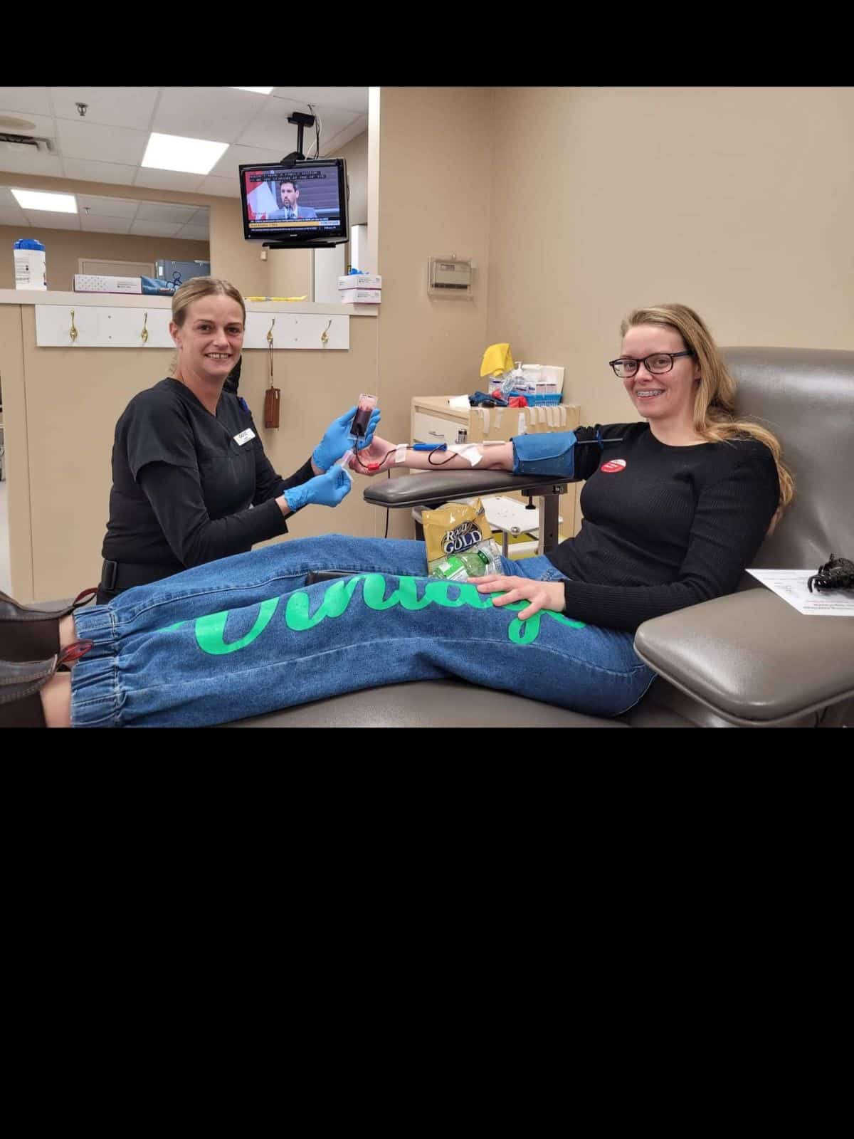A girl sitting in a chair donating blood, with a nurse sitting beside her.