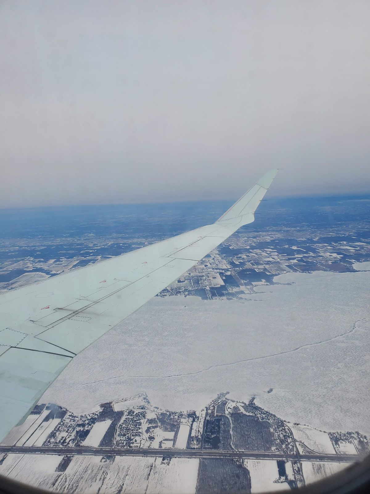 The view from a plane window. A snowy landscape below and the plane wing.