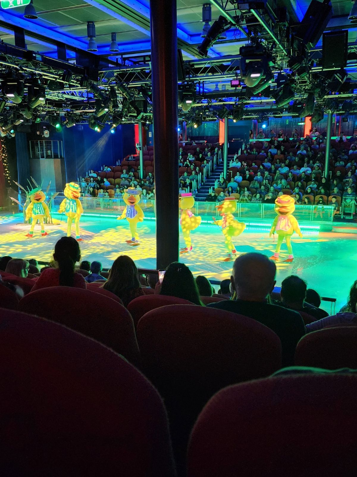 A view of the Frozen in Time show on the Oasis of the Seas. 6 people are dressed up like ducks and are twirling around on ice skates.