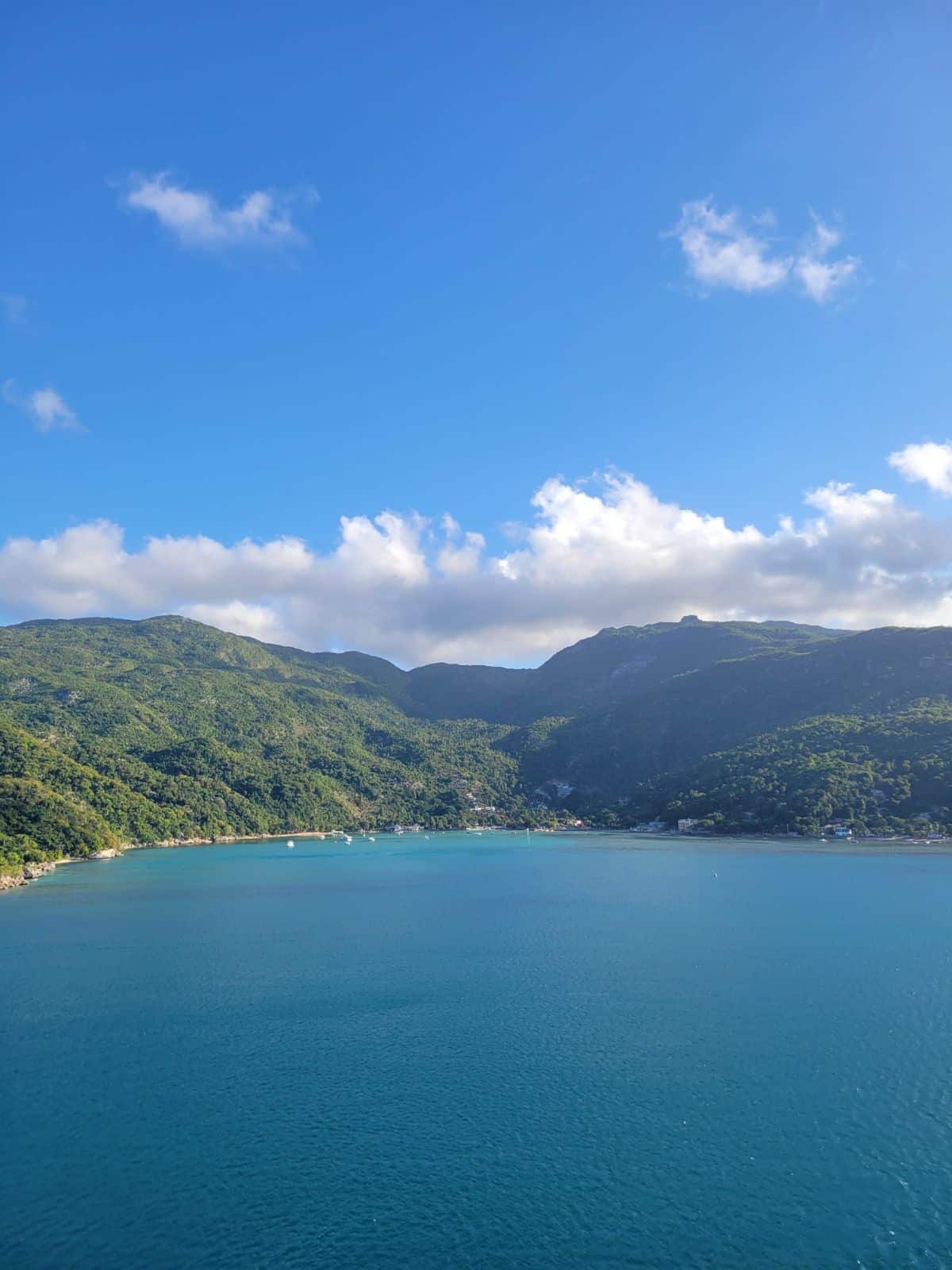 A view of Haiti as the cruise ship is leaving the port. You can see the sky, the green hills of the island the blue water below.