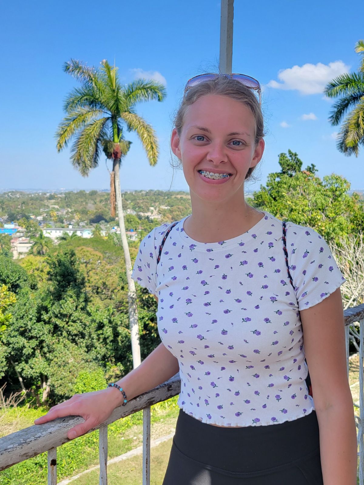 A girl is smiling at the camera with Cuba, palm trees and the blue sky in the background. 