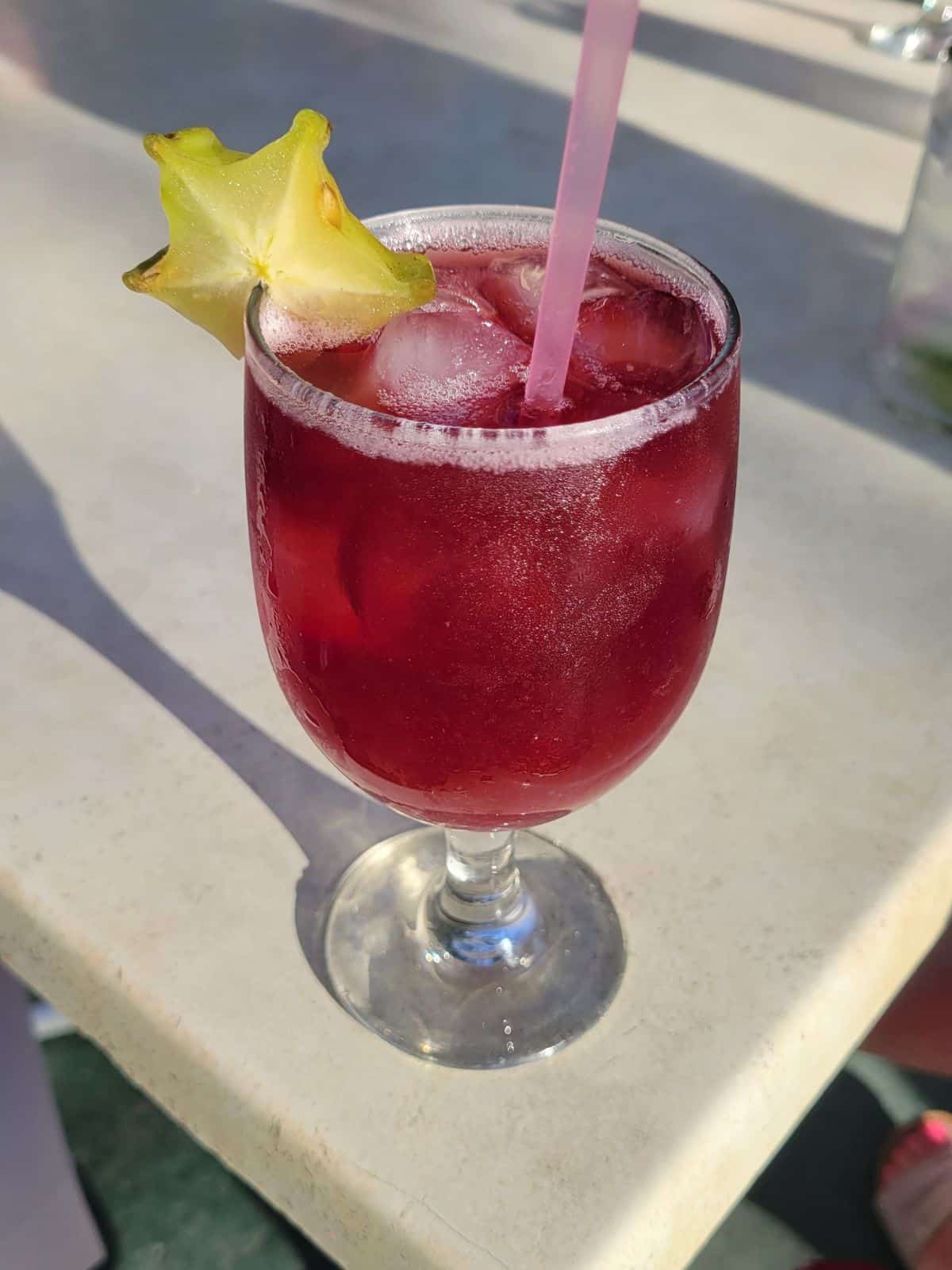 A glass of sangria with a pink straw and a garnish of starfruit on the rim of the glass.