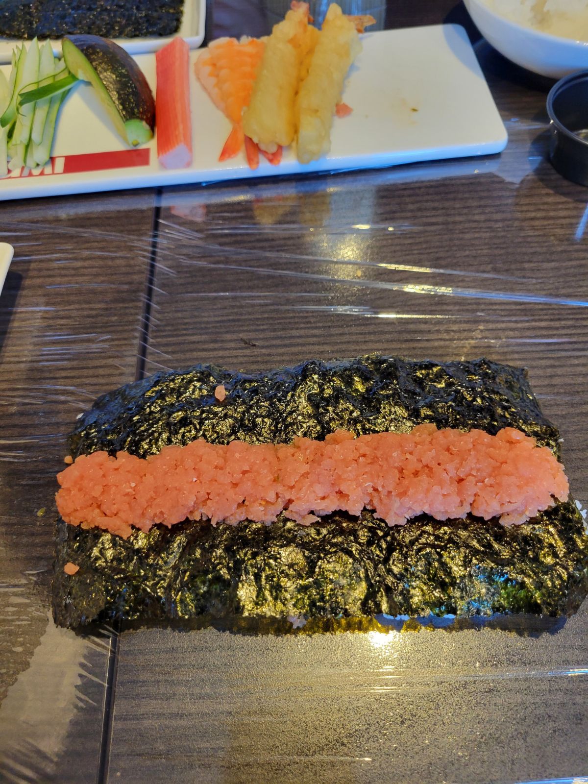 A sushi roll being made. A sheet of seaweed with a line of ground crab in the center. 