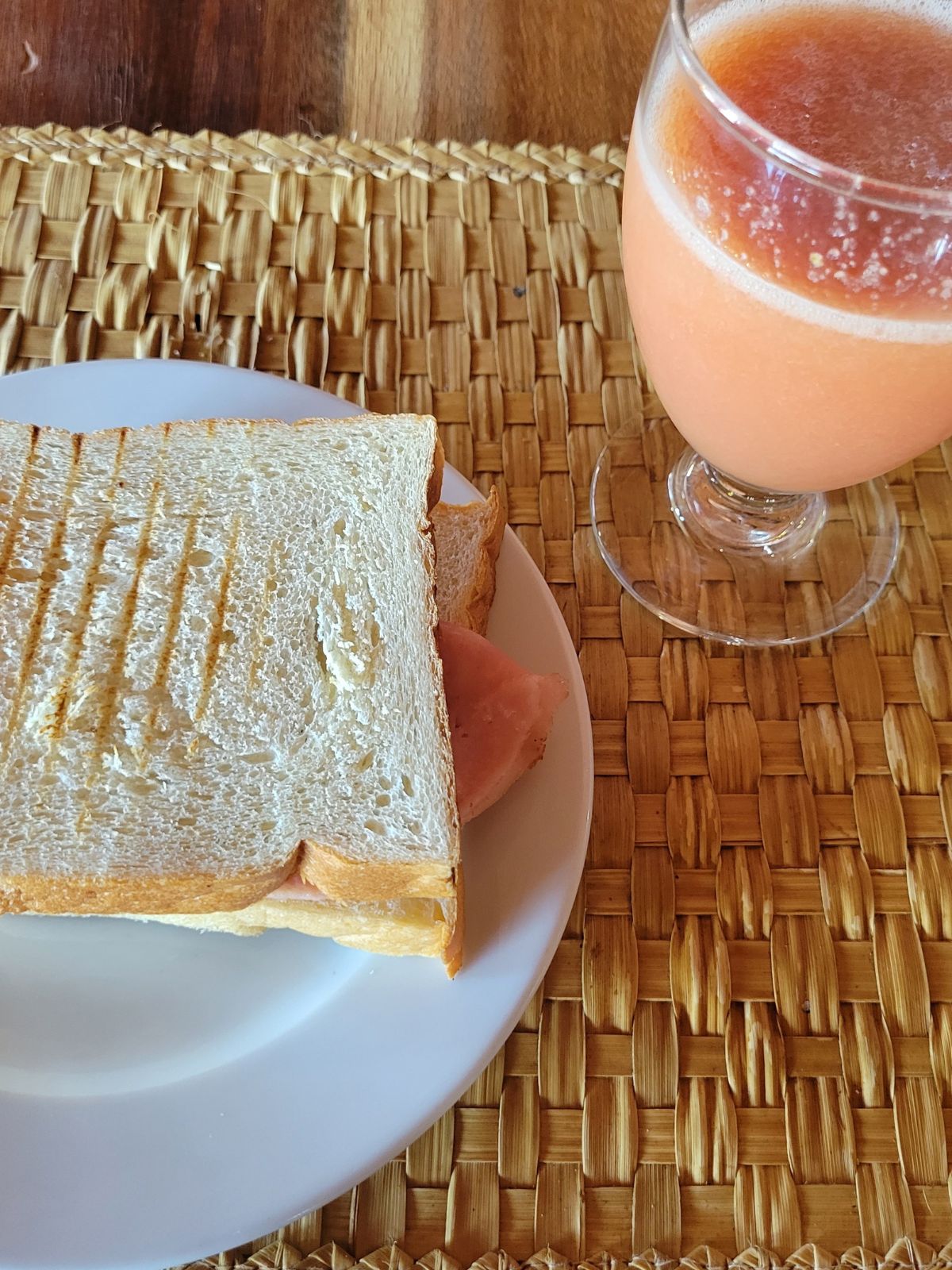 A ham and cheese sandwich on a plate and a fruit smoothie in a glass.