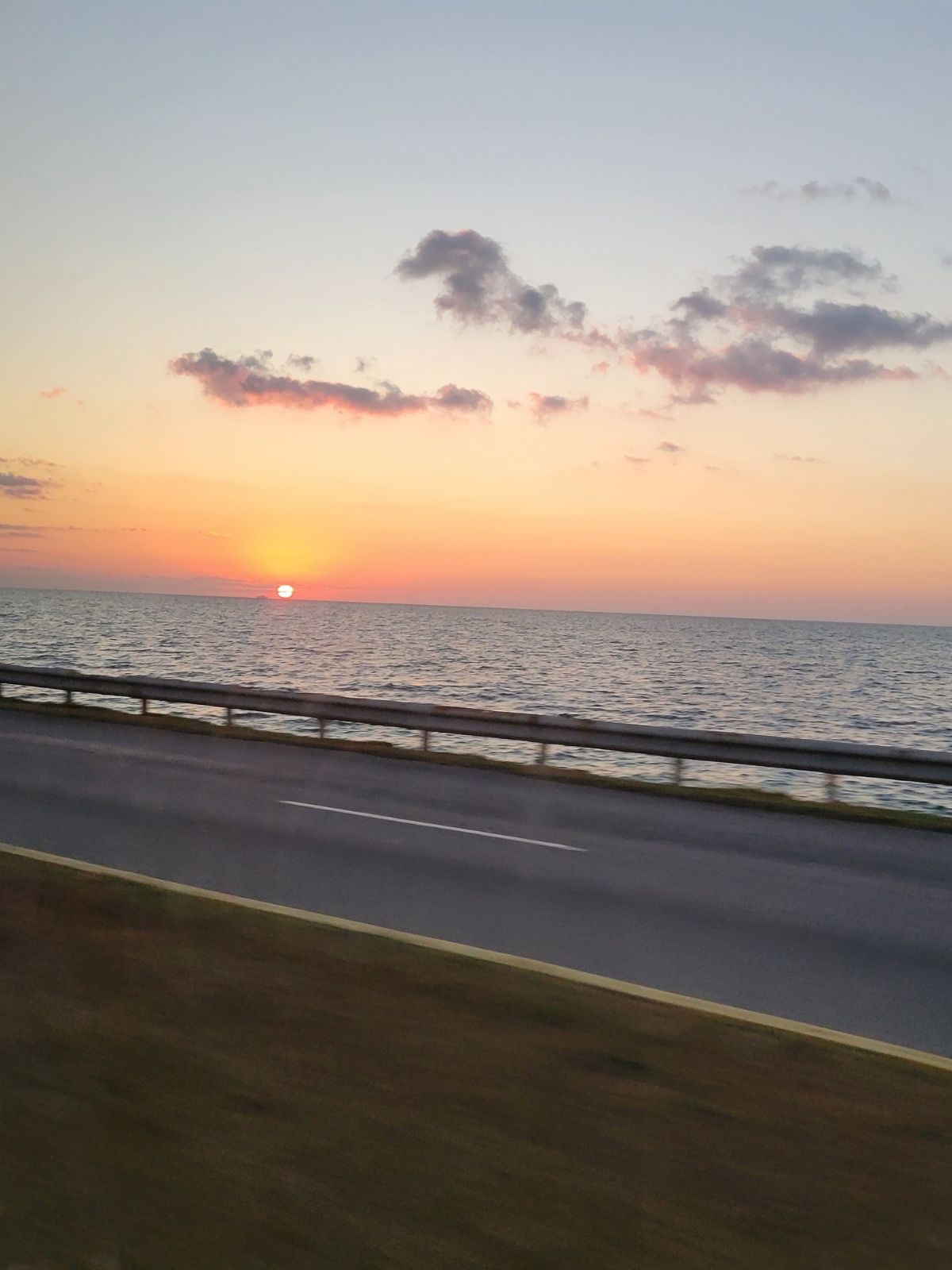 A view of the sunrise over the ocean through the window of a moving bus.